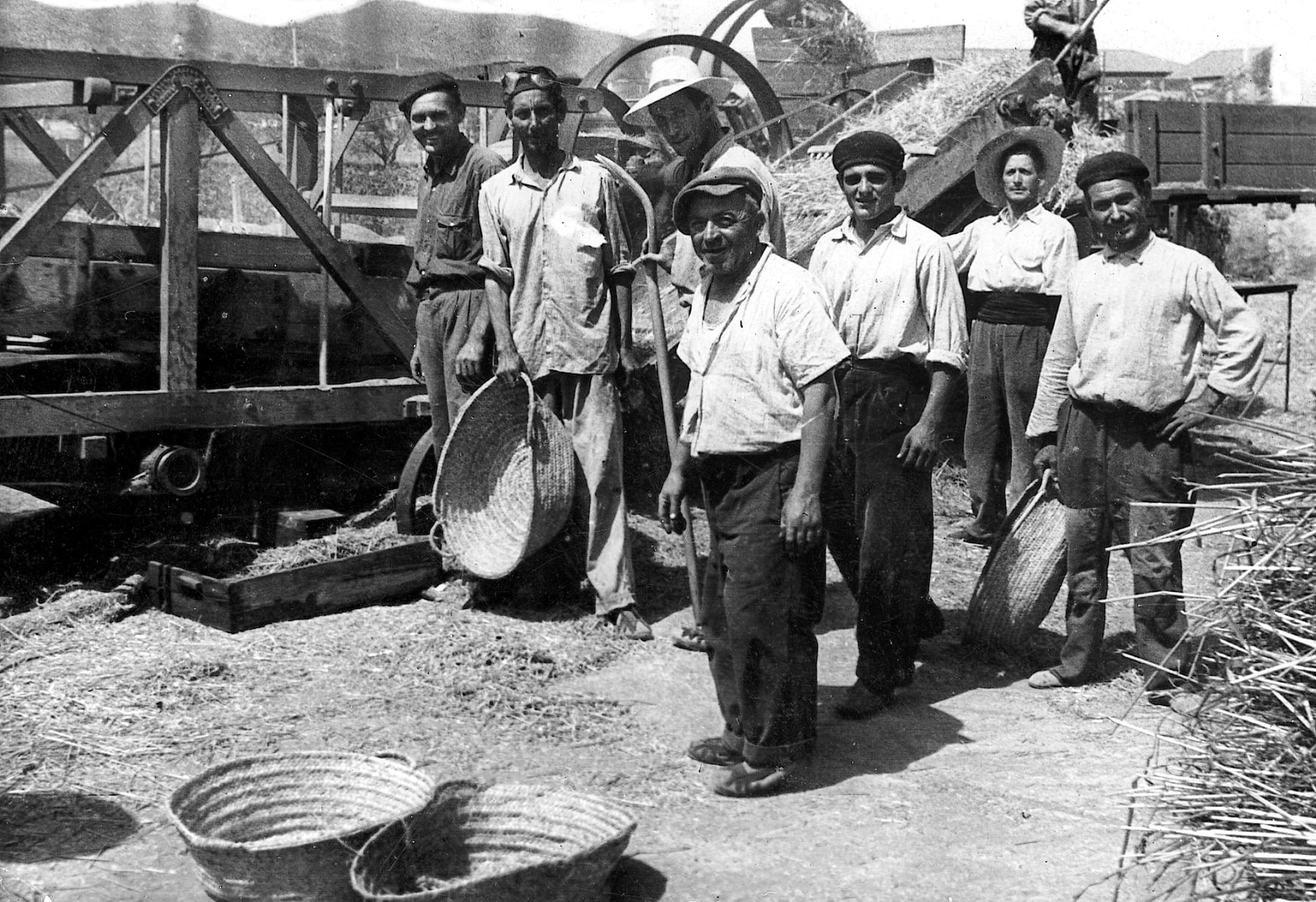 Treballadors del camp davant la màquina d'empaquetar palla