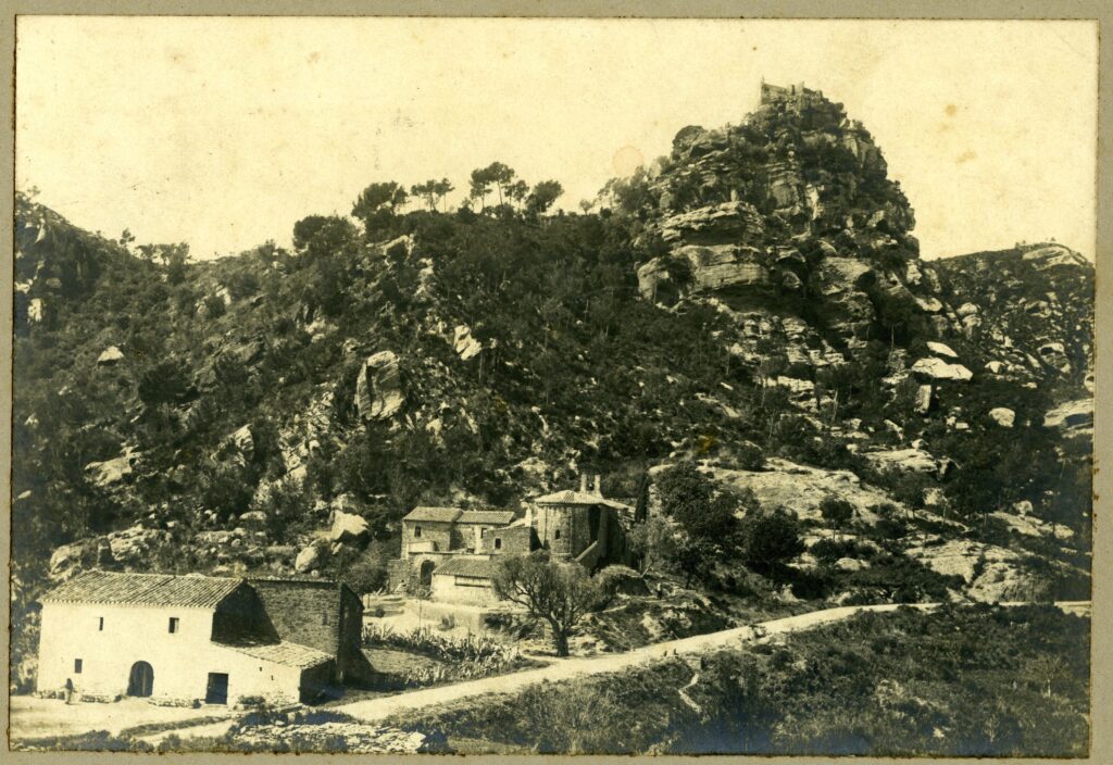 Vista del Castell d'Eramprunyà des de la carretera de Begues, amb can Ramoneda i l'ermita de Bruguers en primer i segon pla, respectivament